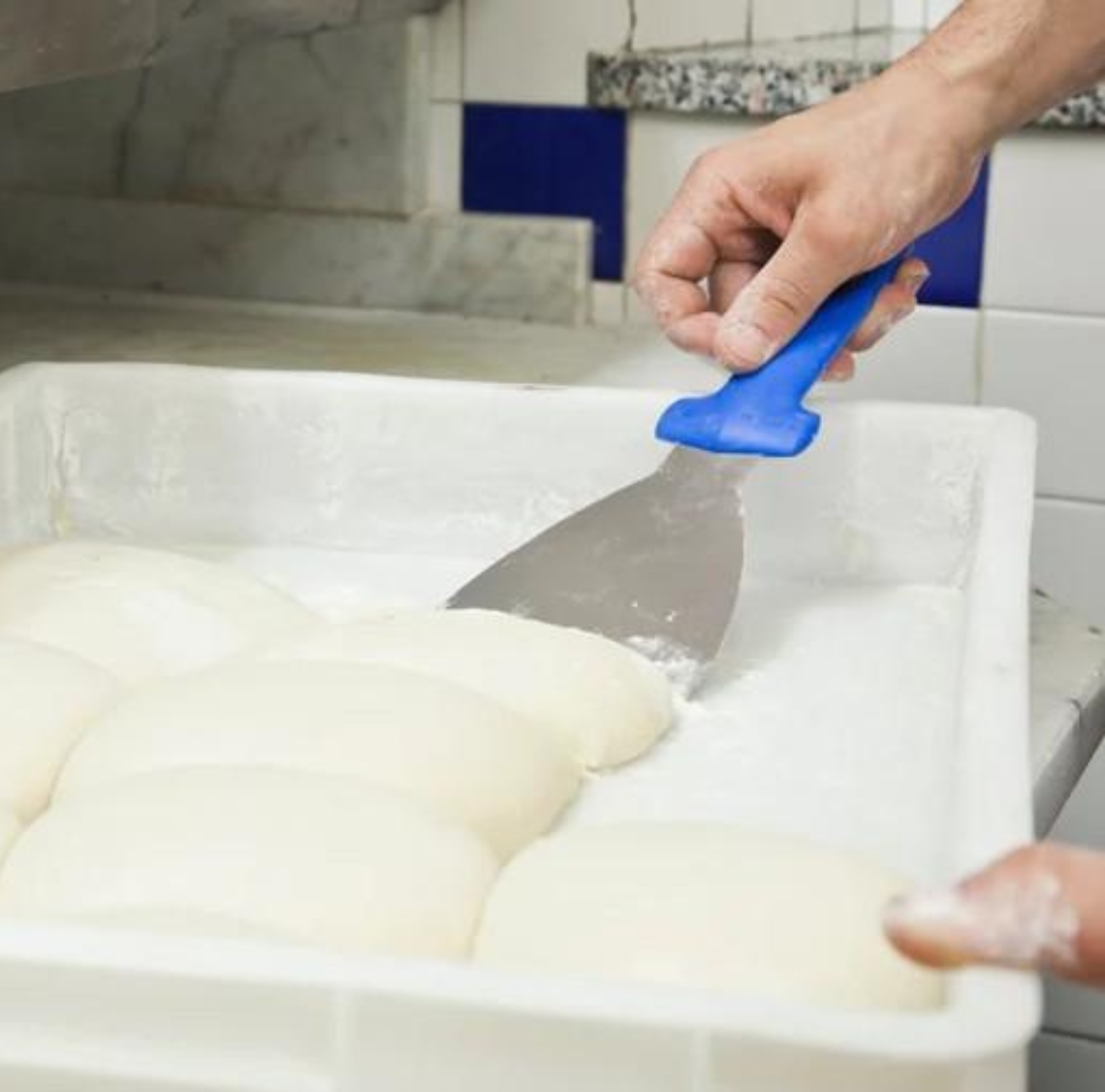 pizza hlebčki v pizza boxu za testo, ter roka ki z lopatko poskuša vzeti testo iz boxa